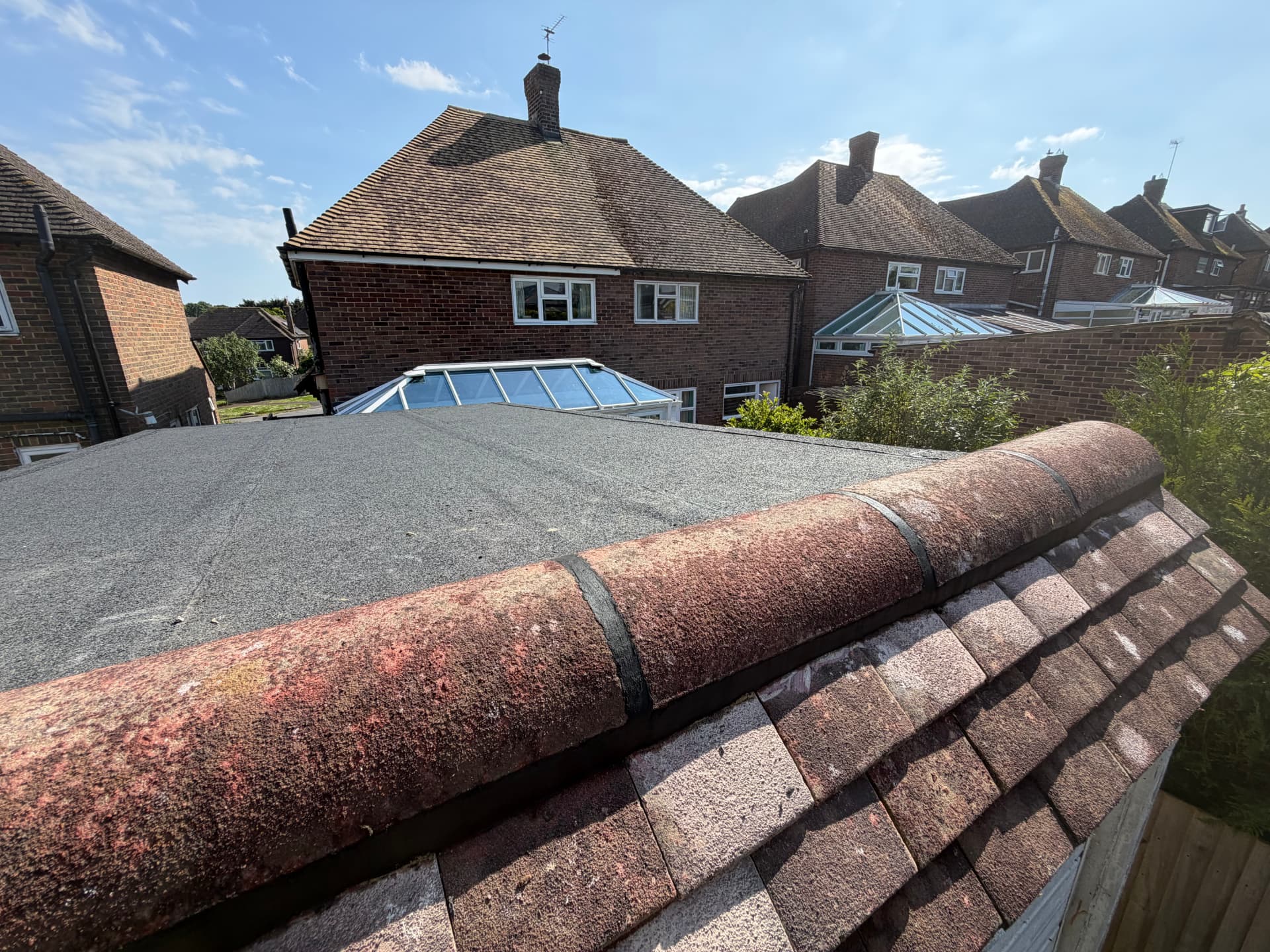 Grey felt roof meeting a red tiled pitched roof on a pair of semi-detached houses